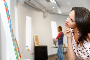 Young caucasian woman standing in art gallery front of  paintings