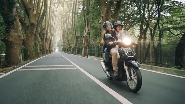 Slow motion shot (60fps) of young Caucasian couple riding their scooter through forest. Shot from front.