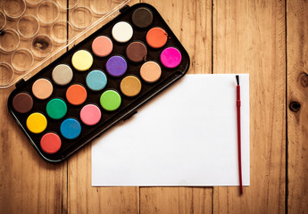empty paper with paintbrush and colorful  color box on wooden ta