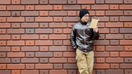 An Asian Man in a Brown Jacket with a Small Notebook 