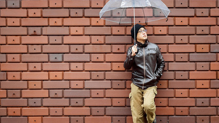 Fototapeta na wymiar An Asian Man in a Brown Jacket With a Clear Umbrella