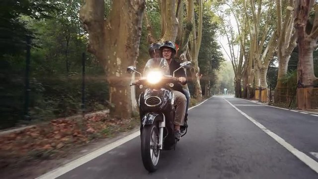 Slow motion shot (60fps) of young Caucasian couple riding their scooter through forest. Shot from front.