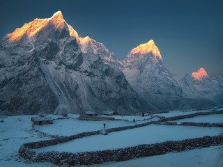 The place where the light is being born. Trekkers are walking through the snowy meadow. Nepal, Everest region, Dusa village. From left to right: Taboche Peak, Cholatse, Arakam Tse and Lobuche East. - 104041326
