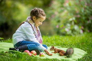 Little beautiful girl sitting on green lawn and feeding squirrel with nuts.  © Suzi Media 