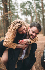 Romantic fairytale wedding couple kissing and embracing in pine forest near retro car.
