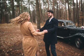 Romantic fairytale wedding couple kissing and embracing in pine forest near retro car.