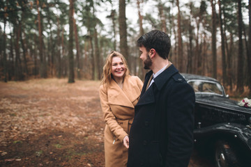 Fototapeta premium Romantic fairytale wedding couple kissing and embracing in pine forest near retro car.