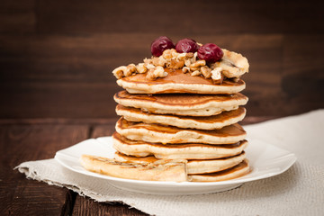 Pancakes with cherries, grilled banana and nuts on a dark background