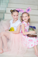 Two cute sisters sitting indoors with bunny ears and flowers celebrate Easter and spring