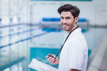 Handsome trainer holding stopwatch and reading clipboard at the pool