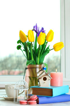 in a vase beautiful and fragrant yellow tulips with green chrysanthemums on a white wooden table and candle with Cup and books against the window