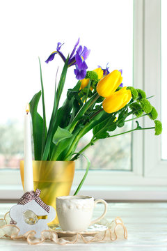 in a vase beautiful and fragrant yellow tulips with green chrysanthemums on a wooden table and a white saucer with a Cup on the background of a window