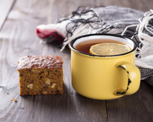 Homemade carrot and banana cake with nuts and spices, a cup of tea with lemon on a wooden surface 