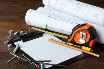 screws of different shapes and roulette with drawings and many other tools on the wooden brown table