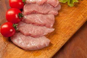 Raw pork оn the wood board. Tomato and lettice