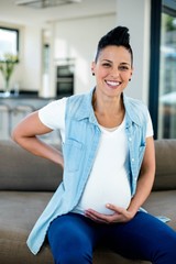 Portrait of pregnant woman sitting on sofa with and on stomach