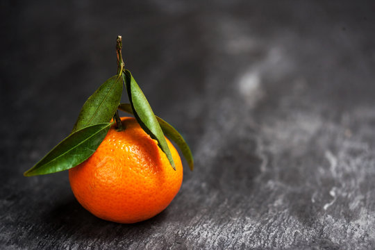 One tangerine with leaf on a black background,