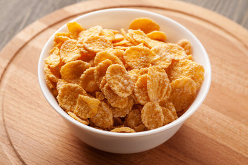 Yellow cornflakes in white bowl on wooden board