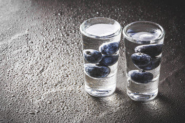 Blueberry vodka shot on wet black surface.