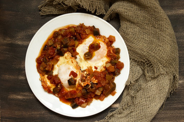Shakshuka and napkin on brown background. Two eggs in tomato sauce with vegetables.
