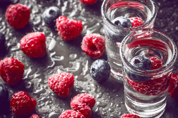 Fototapeta na wymiar Blueberry and raspberry vodka on black surface.