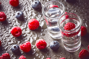 Blueberry and raspberry vodka on black surface.