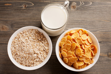 Oatmeal, cornflakes and glass of milk on wooden table