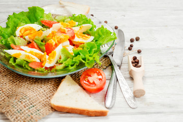 Fototapeta na wymiar healthy salad with fresh vegetables , tomatoes , lettuce , boiled egg and spices and oil on a wooden background