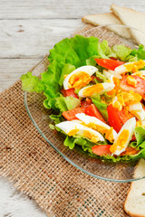 
healthy salad with fresh vegetables , tomatoes , lettuce , boiled egg and spices and oil on a wooden background