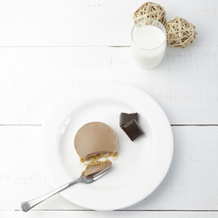A piece of homemade chocolate pie and a small glass with milk on a white wooden table