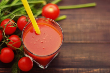 Fresh tomato juice and tomatoes with greens on a wooden table.