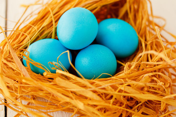 blue  Easter eggs in nest on white wooden background