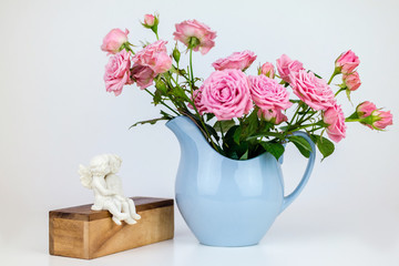 Pink flowers in blue jug. Roses in jug. Two angels on wooden banch.