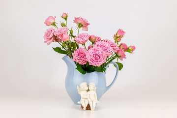 Pink flowers in blue jug. Roses in jug. Two angels on wooden banch.