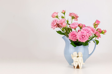 Pink flowers in blue jug. Roses in jug. Two angels on wooden banch.