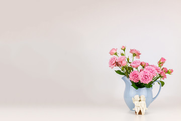 Pink flowers in blue jug. Roses in jug. Two angels on wooden banch.