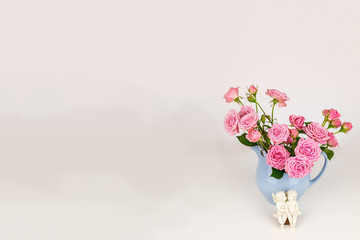 Pink flowers in blue jug. Roses in jug. Two angels on wooden banch.
