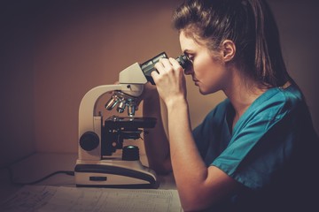 Confident veterinarian examining the test under the microscope in veterinary clinic.