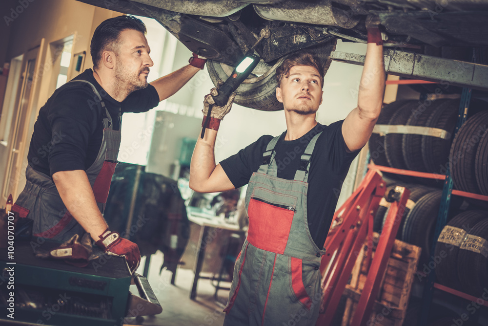 Canvas Prints Professional car  mechanics  working under lifted car in auto re