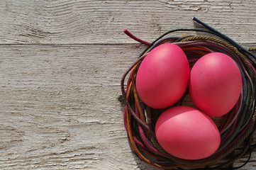 Easter pink eggs  in a nest with bright tapes on an wooden old background