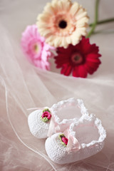 White knit baby booties decorated with flowers and ribbons  with gerberas in the background