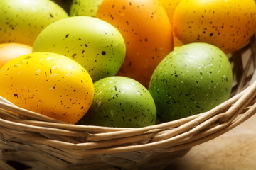 easter eggs painted in orange, yellow and green in a basket, clo