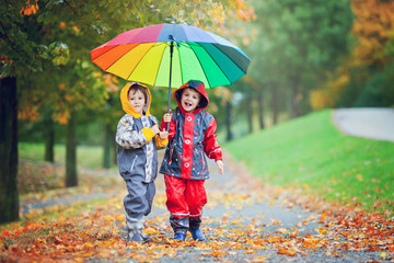Two adorable children, boy brothers, playing in park with umbrel