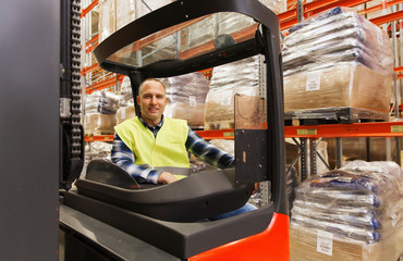 Obraz na płótnie Canvas smiling man operating forklift loader at warehouse