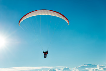 Paraglider flying over the clouds - into the sun