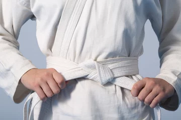 Rolgordijnen Vechtsport Handen die witte riem aanhalen op een tiener gekleed in kimono voor vechtsporten