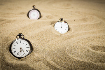 Trois montres à gousset réparties dans le sable d'une plage