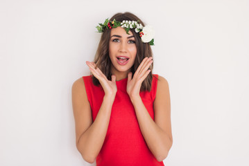 Naklejka premium beautiful young girl in a red dress flower wreath on her head on a white background is experiencing delight