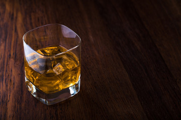 Glass of scotch whiskey and ice on a wooden background with copyspace