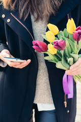 Young woman in coat holding a bouquet of tulips in one hand and